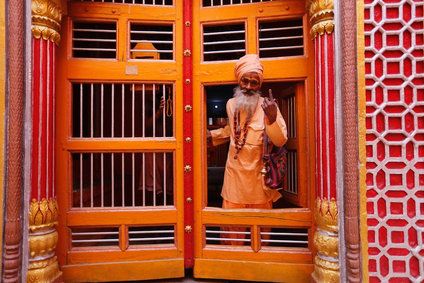 A man holds up his finger while stepping through a yellow, orange and gold doorway