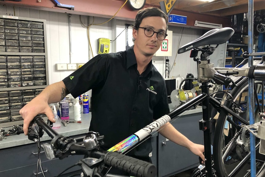 Jamie Holton poses in a workshop with a bike on a stand.