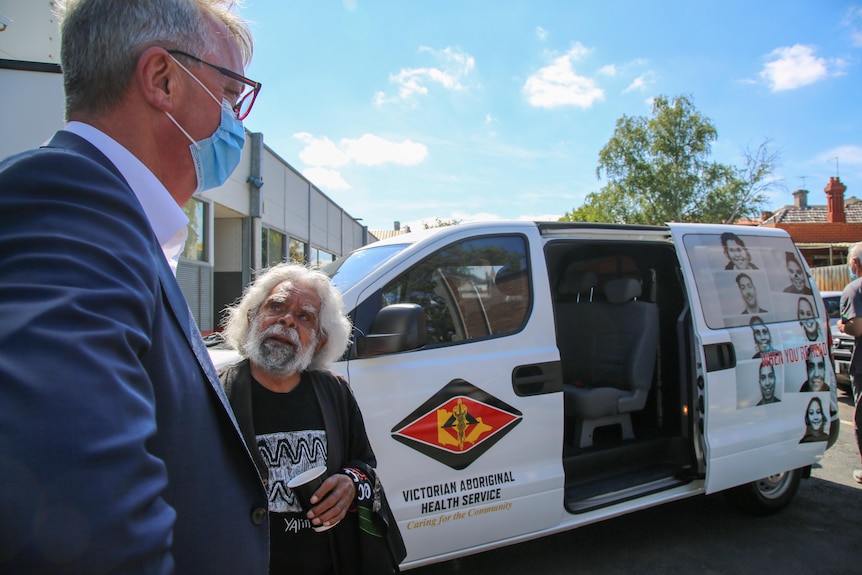 Uncle Jack Charles speaks with a masked Martin Foley outside a Victorian Aboriginal Health Service van.