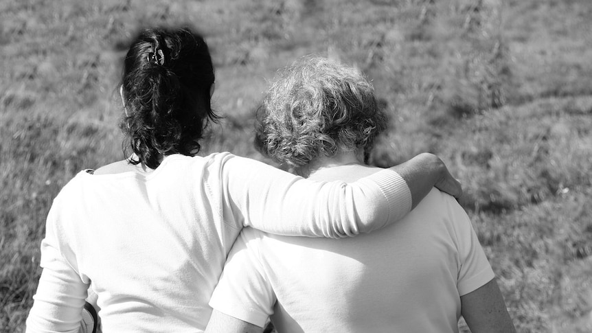 Daughter with arm around her mother in a field.