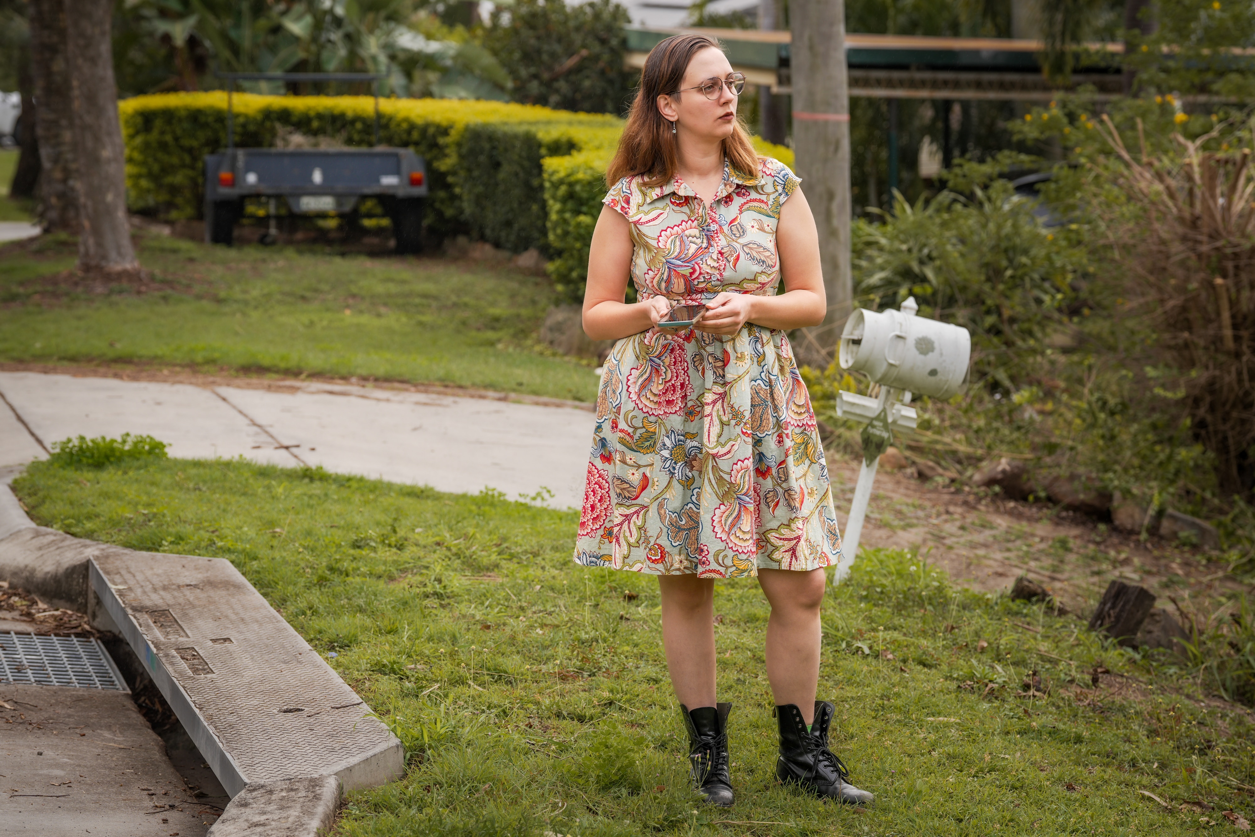 A woman in a floral dress holds her phone on the street looking at houses