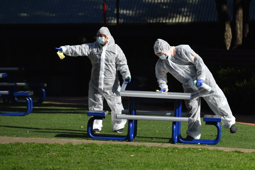 Two people in full PPE clean a table at school grounds