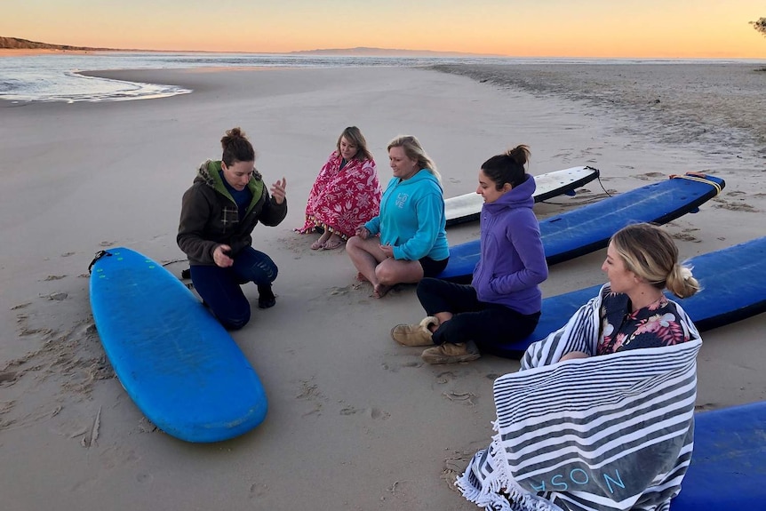 A surfing instructor and four other people sit on a beach at Noosa on Queensland's Sunshine Coast.