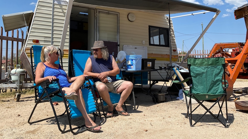 a woman and man sit on chairs in front of a caravan