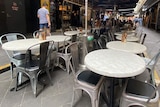 Round cafe tables lined up down a laneway are empty.