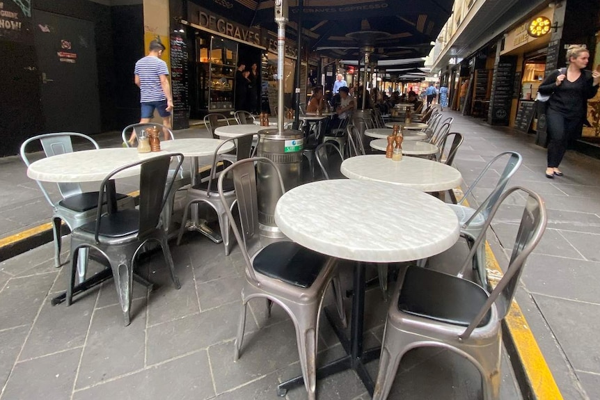 Round cafe tables lined up down a laneway are empty.