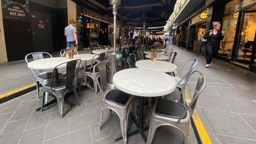 Round cafe tables lined up down a laneway are empty.