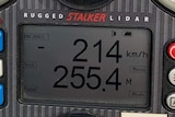 A radar gun shows a detected speed of 214 kilometres per hour. In the background, a car is pulled over on the side of the road.