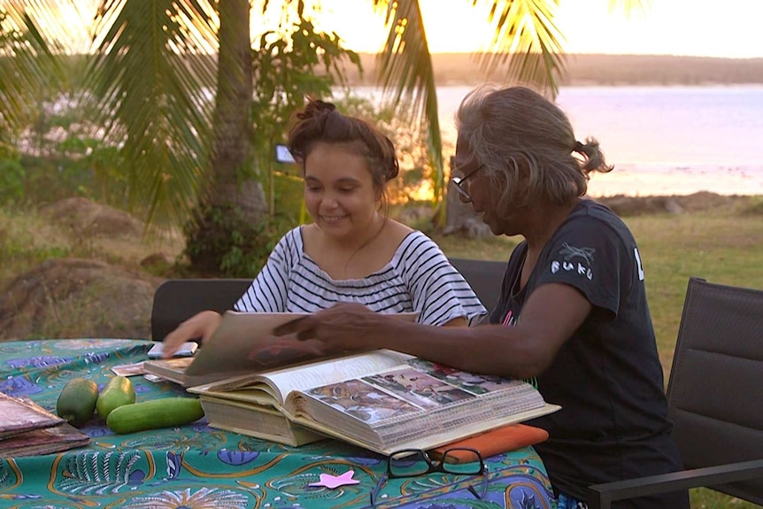 Young woman and mother sitting at table outside looking at photo albums at sunset.