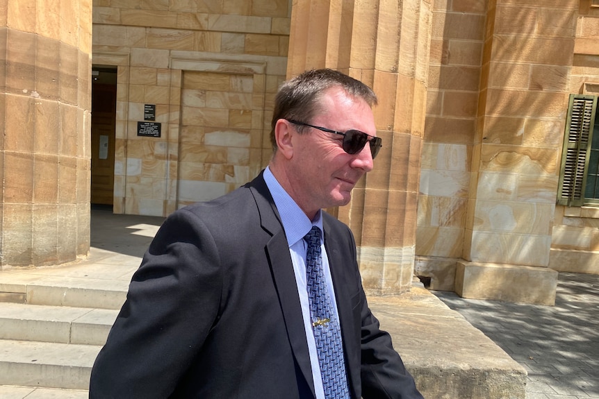 Ronald Maurer, wearing a suit and sun glasses, walking outside a court building