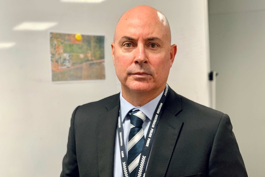 Image of a bald man wearing a lanyard around his neck, he's wearing a dark suit and tie.