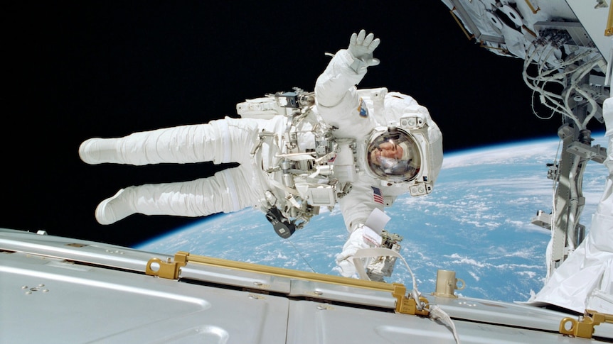 astronaut floating in space horizontally above a white space shuttle