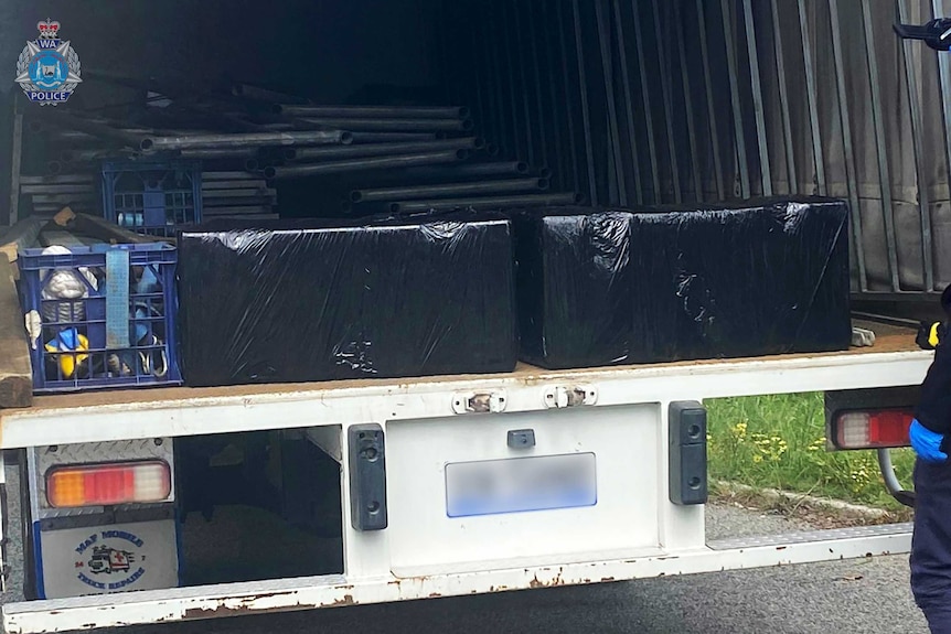 The back of a large truck showing tubs wrapped in black plastic next to a crate.