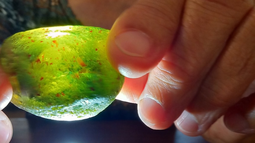 A close-up of hands holding a large green and yellow rock