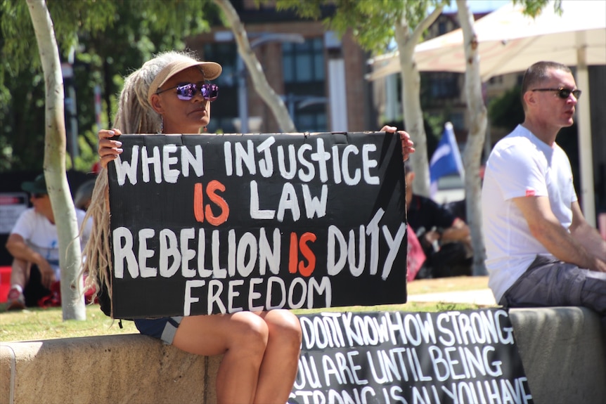 A woman holds a sign at a Perth protest saying "When injustice is law, rebellion is duty".