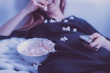 A woman lying on bed while eating popcorn