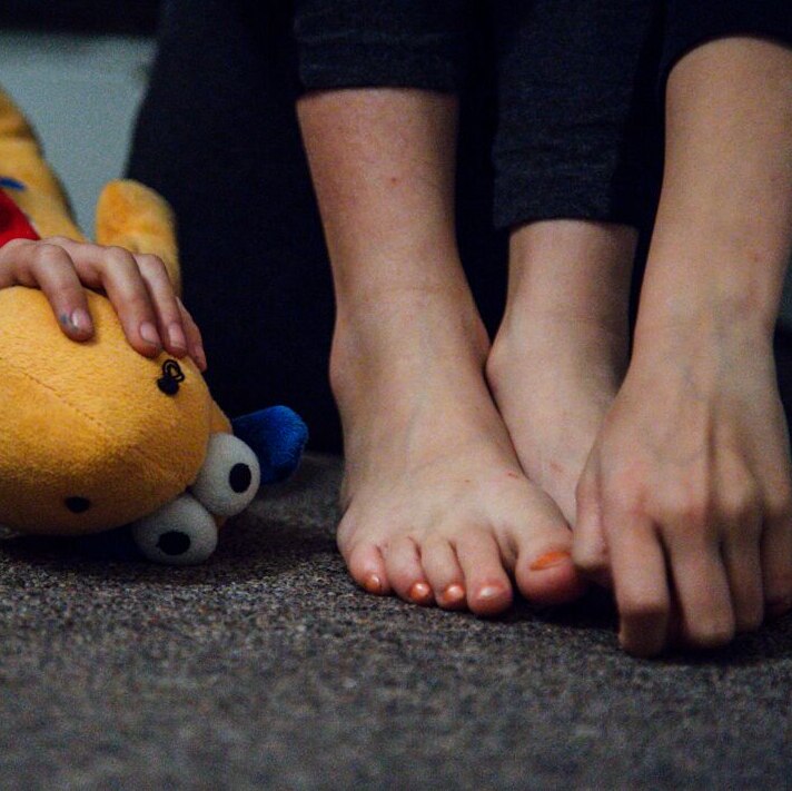 A woman's hand on her bare feet next to a child's hand on a toy.
