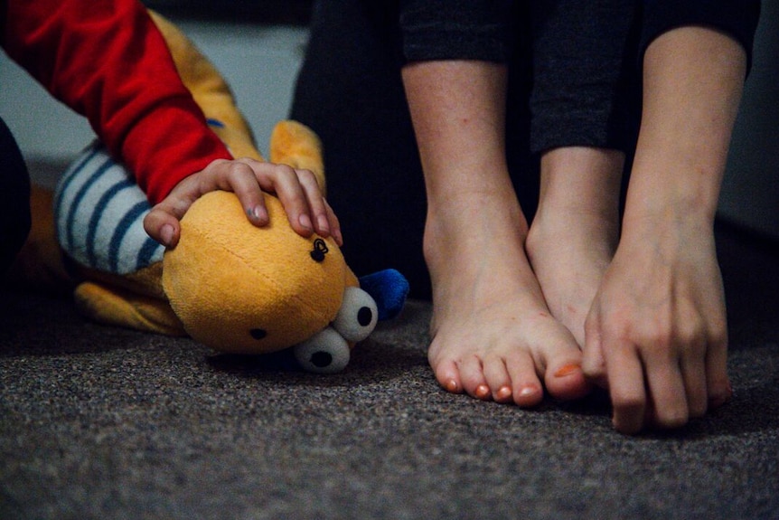 A woman's hand on her bare feet next to a child's hand on a toy.