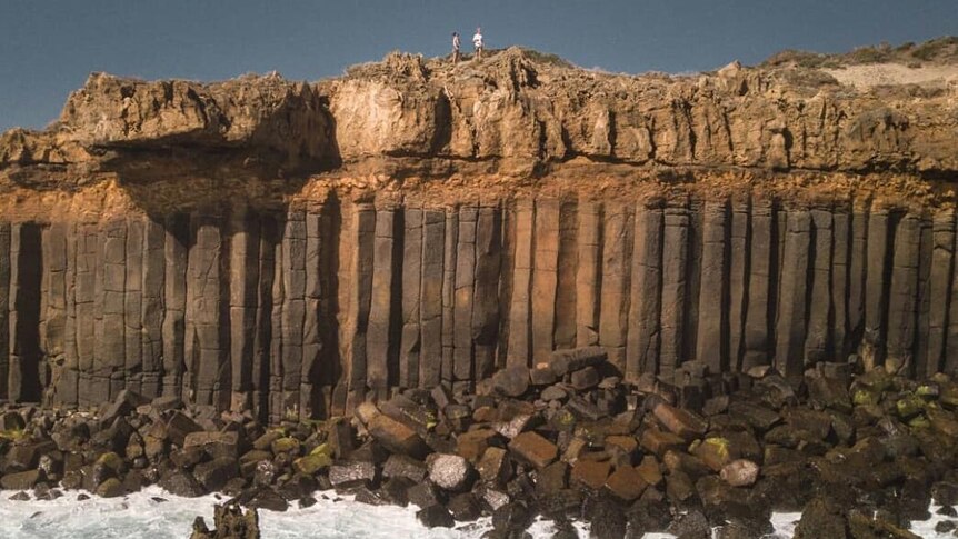 Two people stand on top of basalt column cliffs.