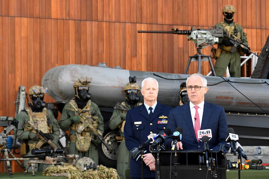 Heavily armed soldiers and a sniper rifle are seen behind Prime Minister Malcolm Turnbull as he speaks to the media.