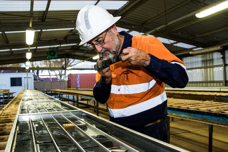 A geologist in a hard work hat and overall inspects drilling samples