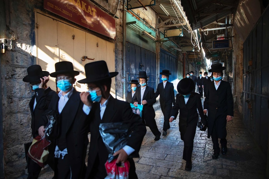 A group of ultra-Orthodox Jewish youth wear protective face masks as they walk down the street.