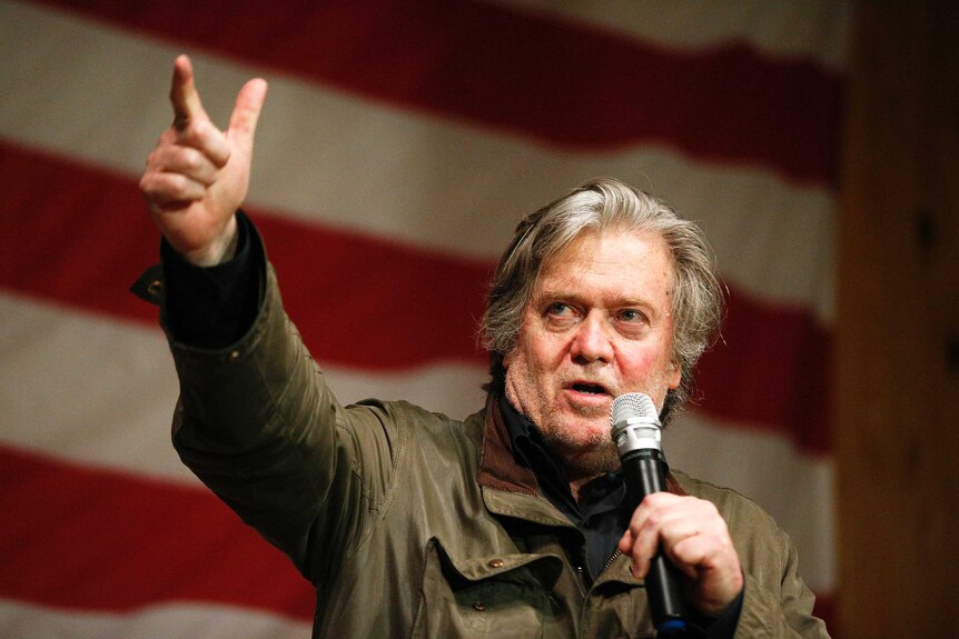 Steve Bannon stands in front of an American flag as he gestures during a speech.