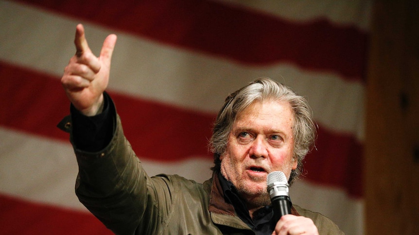 Steve Bannon stands in front of an American flag as he gestures during a speech.