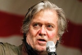 Steve Bannon stands in front of an American flag as he gestures during a speech.