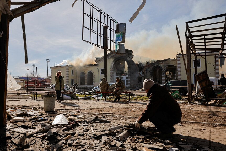 Smoke rises from a train station hit by a Russian missile strike in Ukraine as people stand nearby