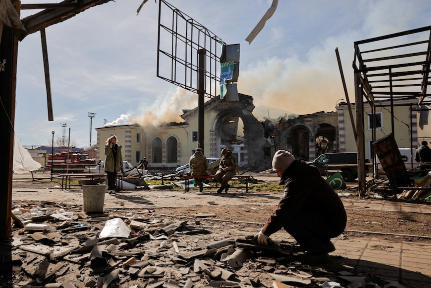 Smoke rises from a train station hit by a Russian missile strike in Ukraine as people stand nearby