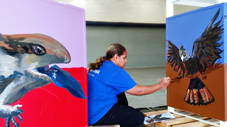 An Aboriginal girl paints a mural of a cockatoo