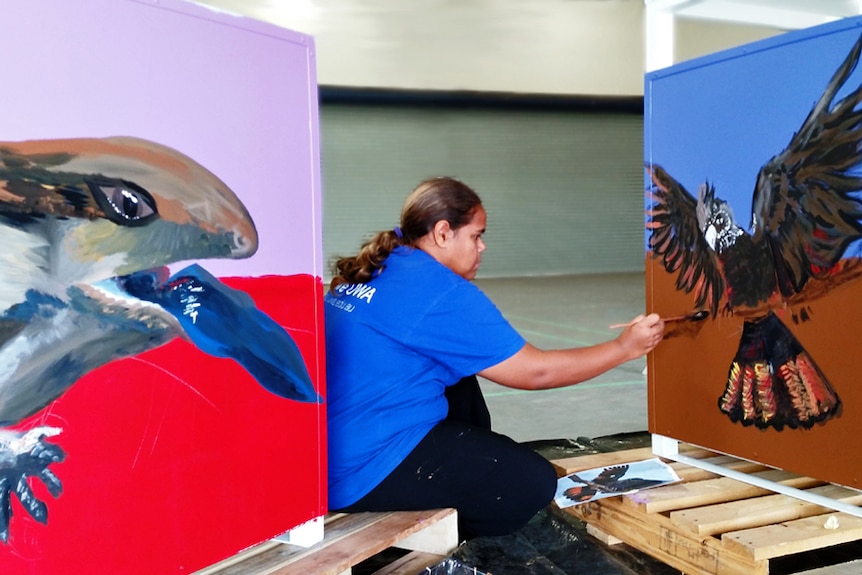 An Aboriginal girl paints a mural of a cockatoo
