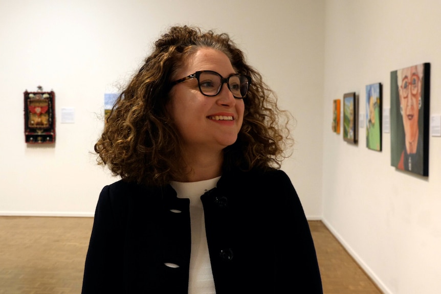A beautiful woman with curly hair looks happily at artworks in the gallery