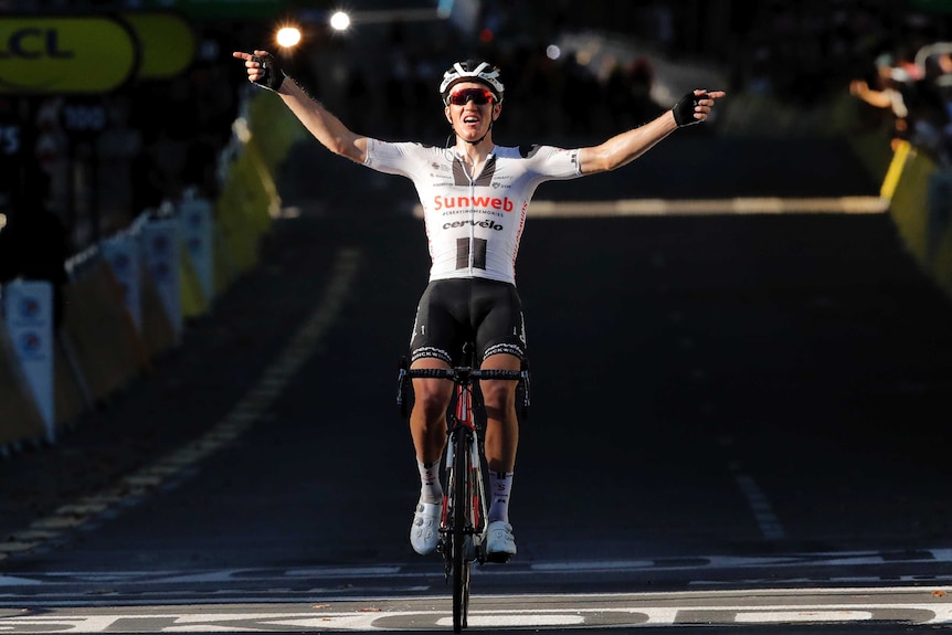 A cyclist sits up in the saddle and puts his arms out to the side as he celebrates a Tour stage win.