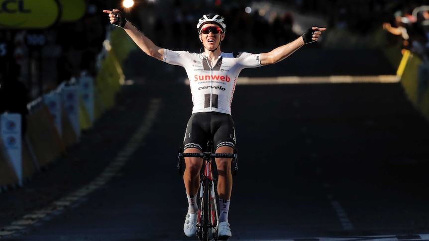 A cyclist sits up in the saddle and puts his arms out to the side as he celebrates a Tour stage win.