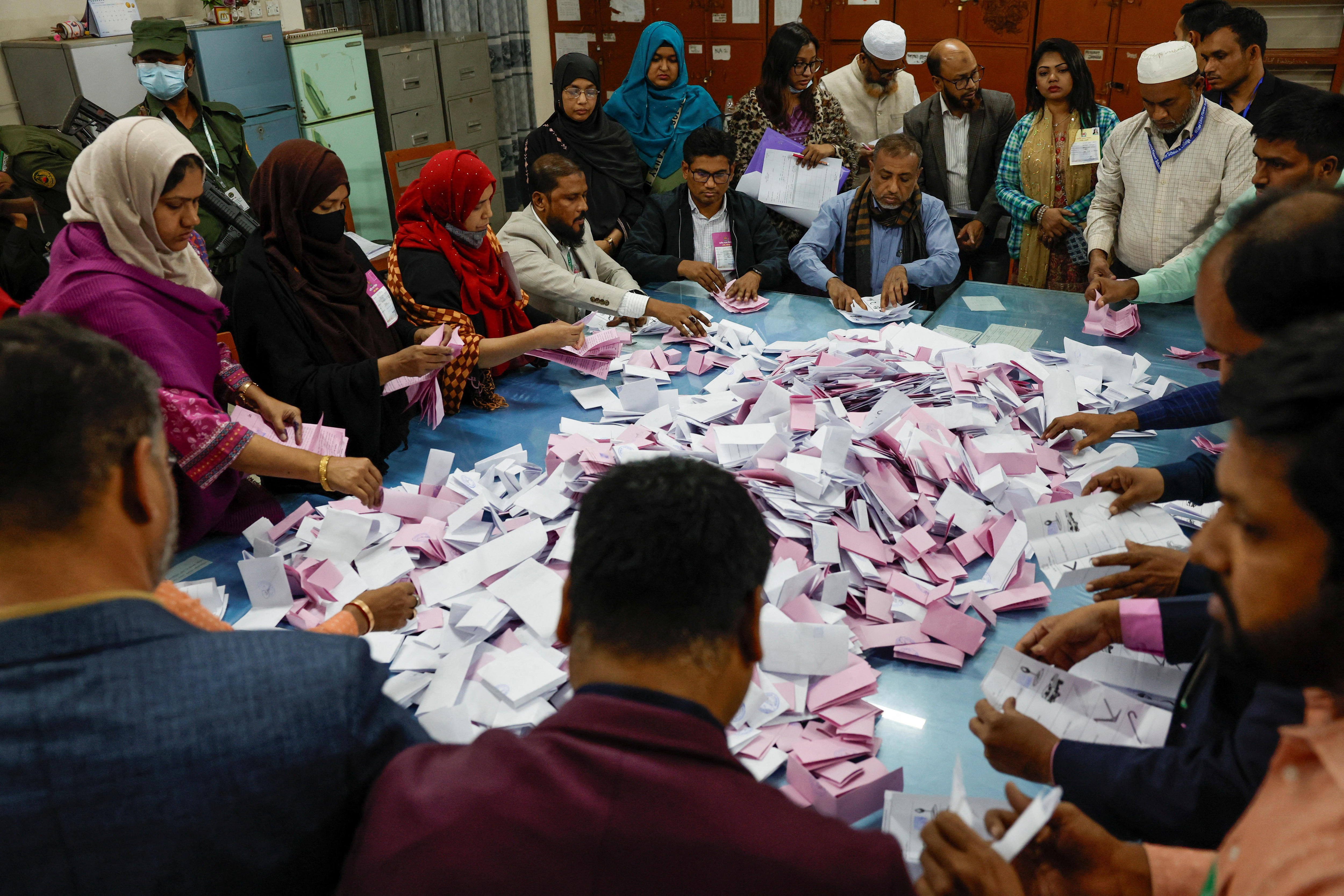 Pink and white slips sit piled on a table as people surrounding it pick them up and count them.