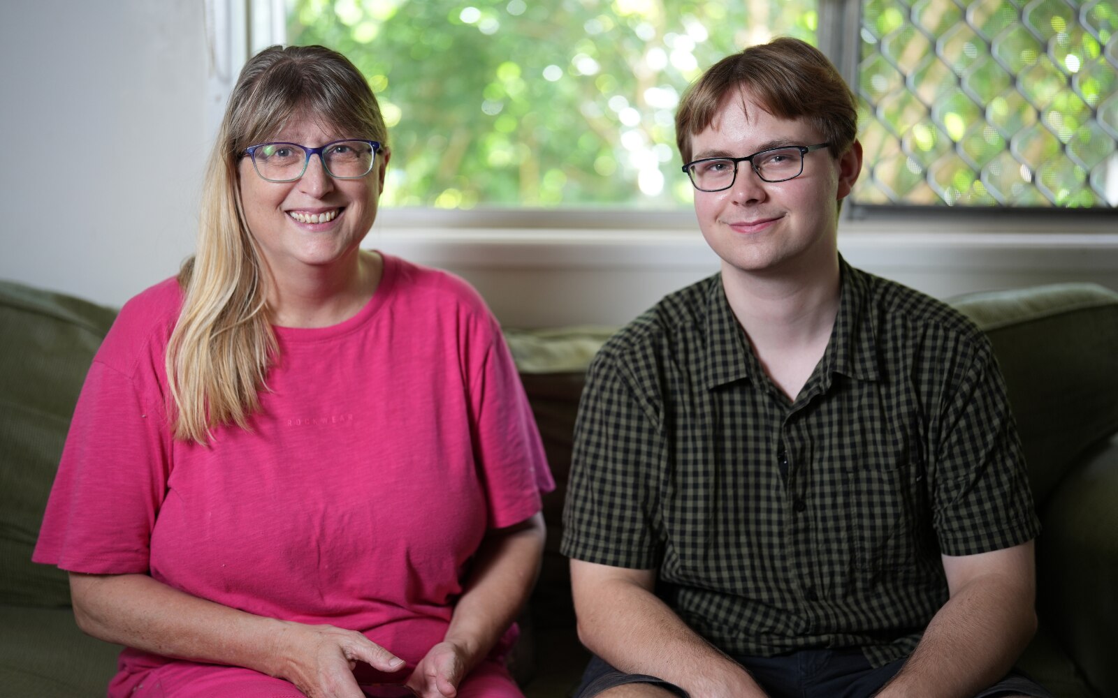 A young white man with short brown hair and glasses sitting with a middle aged white woman with long blonde hair