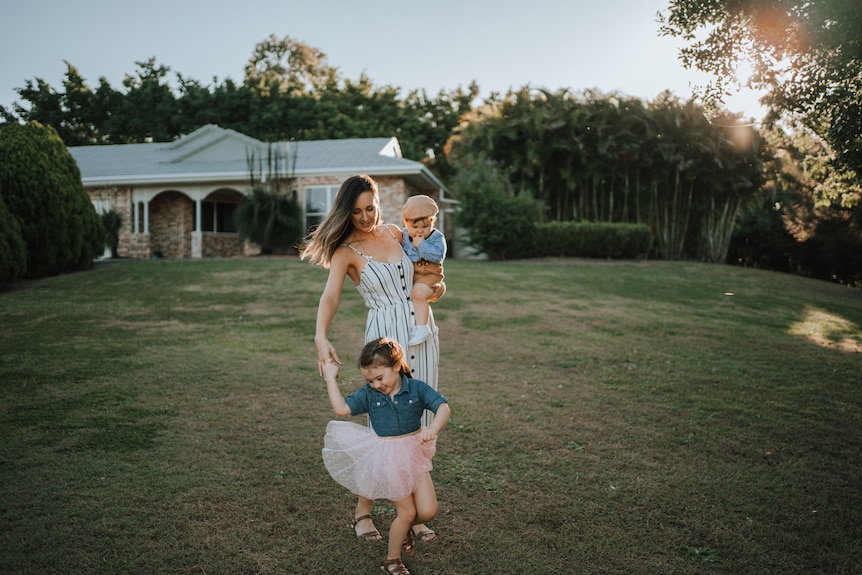 Woman holds her son on her hip while holding onto her daughter who is dancing.