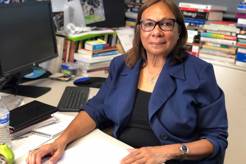 A woman in a blazer sits at a desk in an office