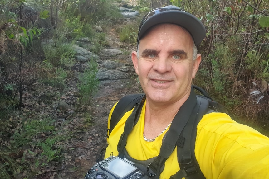 Man in a yellow shirt with a big camera smiles for a seflie.