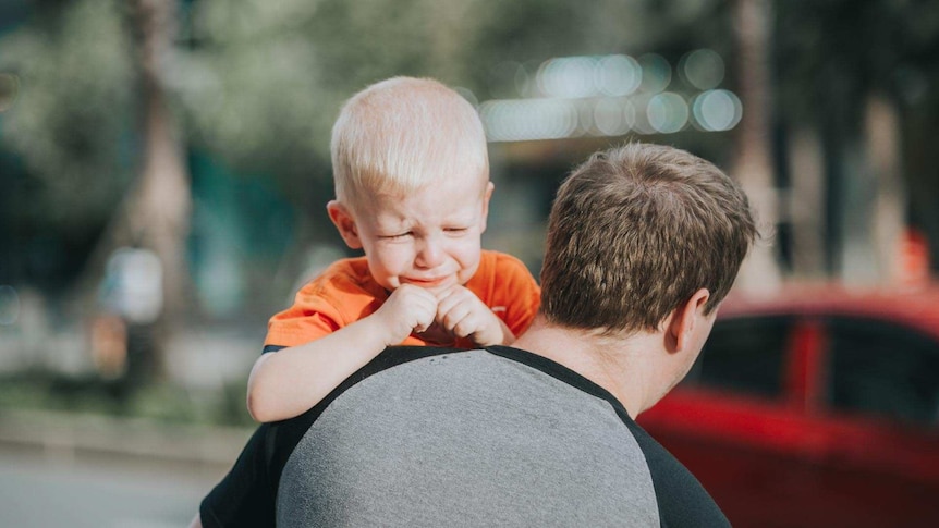 Little boy looking upset as he approaches the car with dad to attend day care