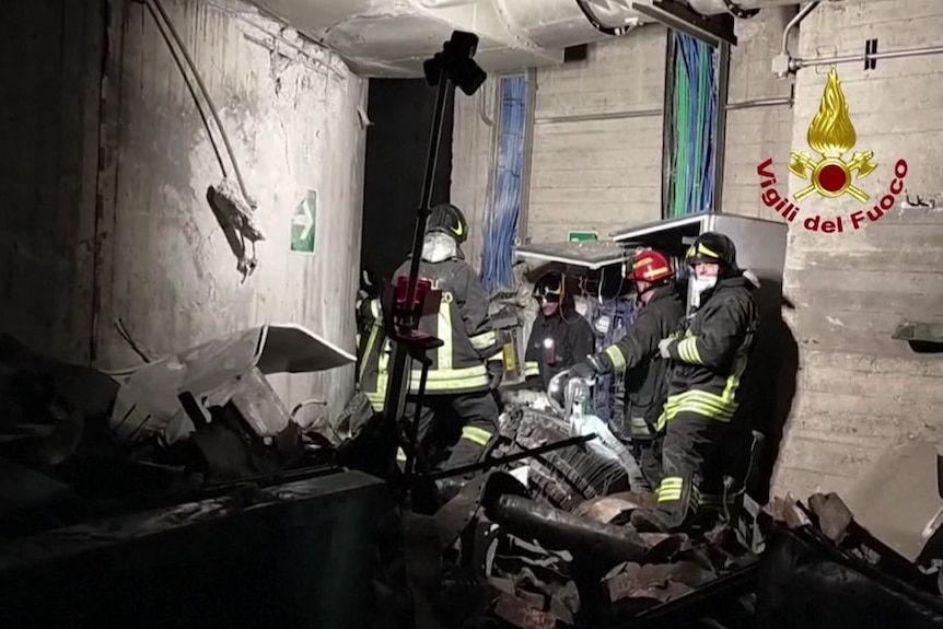 Emergency workers in a concrete chamber surrounded by debris.