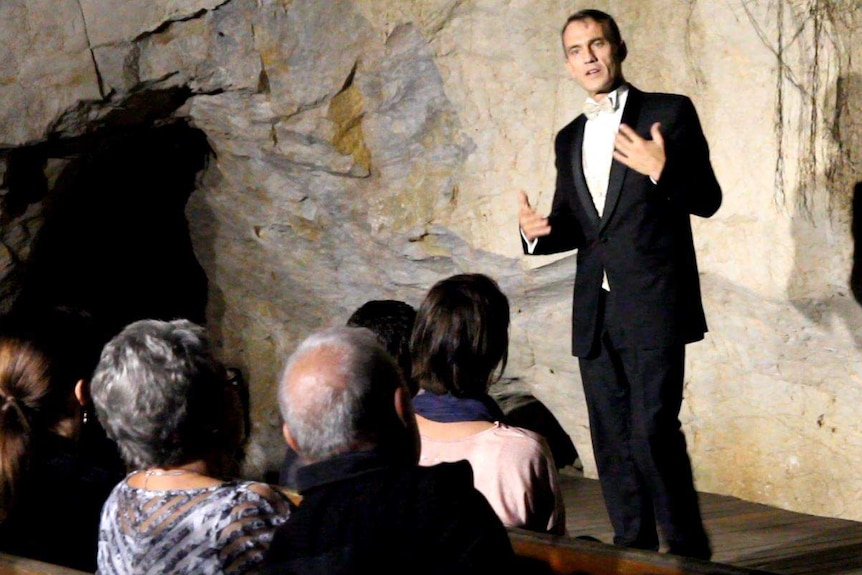 Man stands on a small stage in a cave.