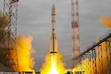 The Proton-M rocket blasts off from the launchpad, with yellow flame coming out of the base of the rocket.