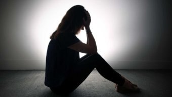 A woman holds her head in her hands against a grey backdrop.