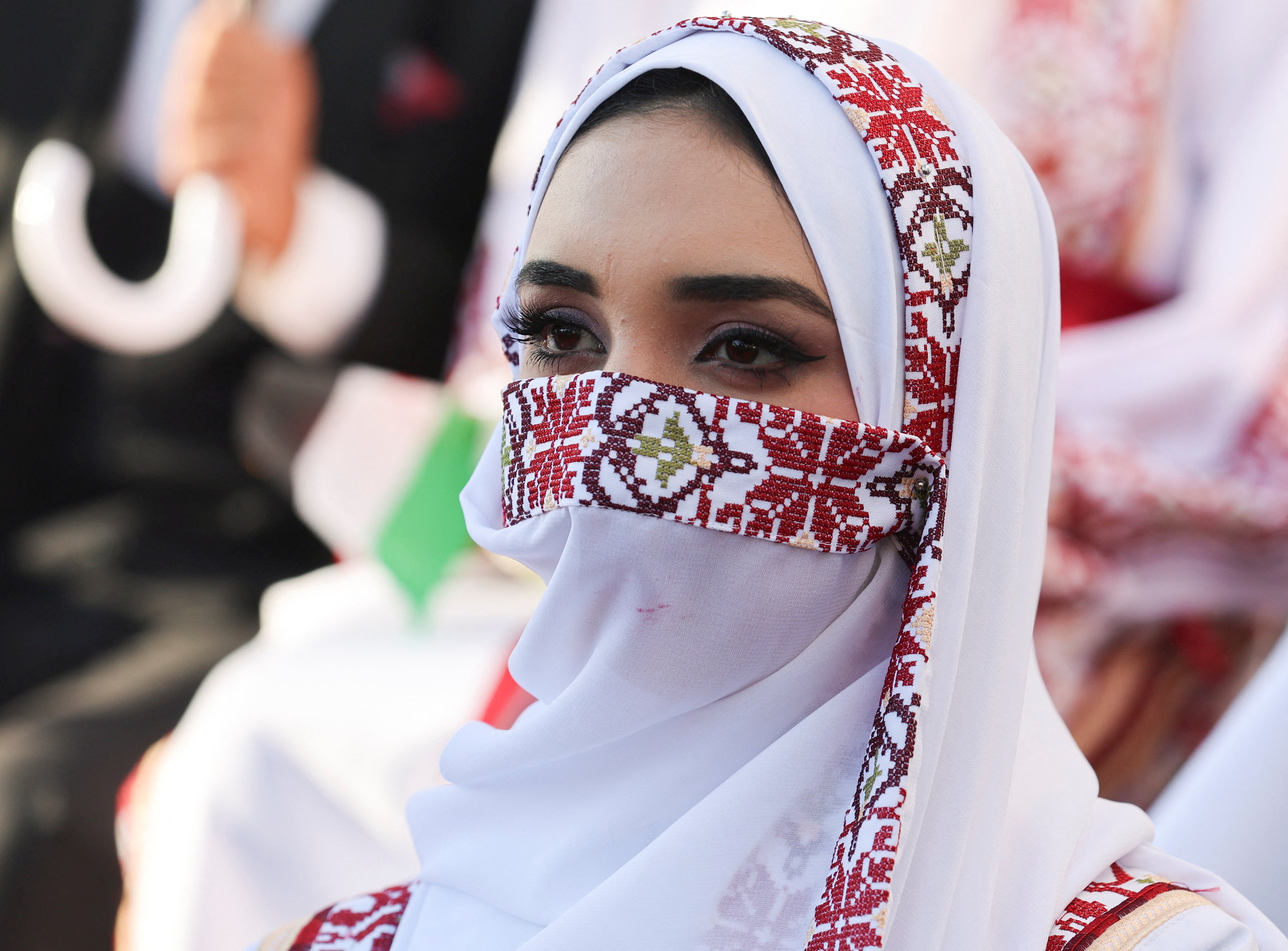 A woman wearing a white hijab with red embroidery covering her hair and mouth but not eyes.