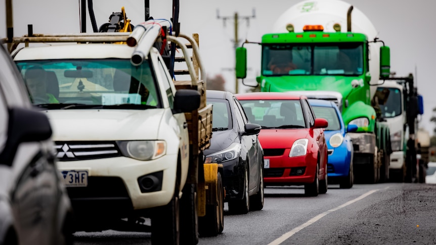 Cars queue on a road under overcast skies.