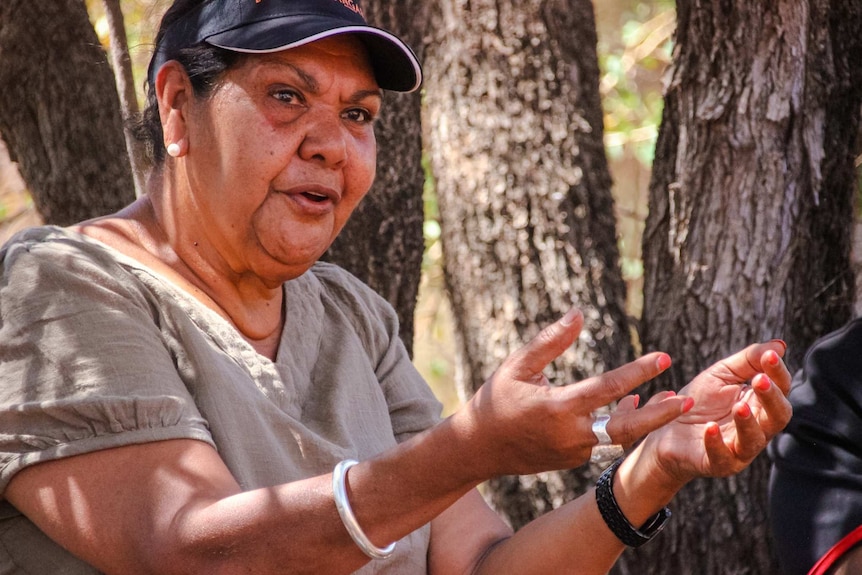 .June Oscar explaining something, with her arms and hands stretched out