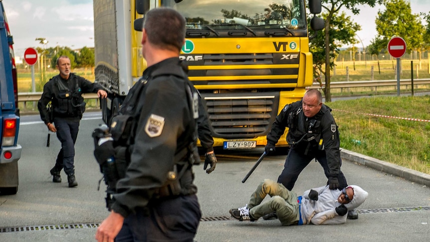 French gendarmes attempt to block a migrant after he entered the Eurotunnel site near Calais